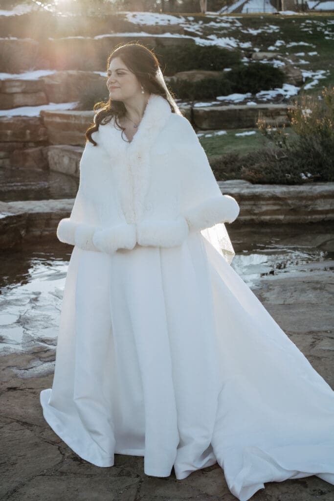 Bride with a winter fuzzy white shall in front of waterfall