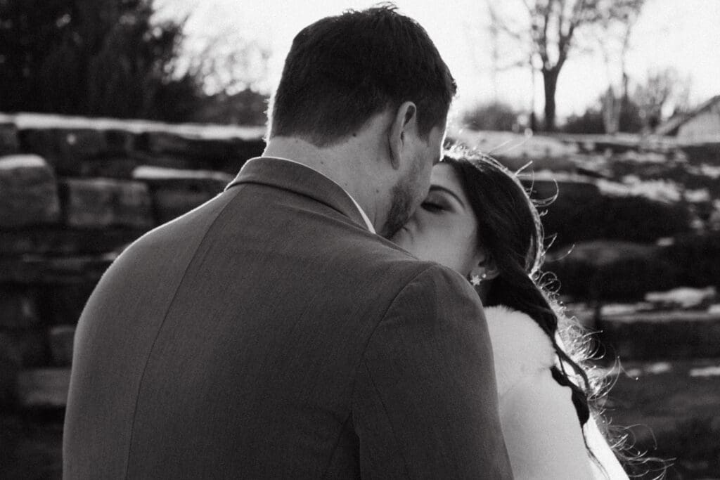 black and white photo of bride and groom kissing from the view over the grooms shoulder

