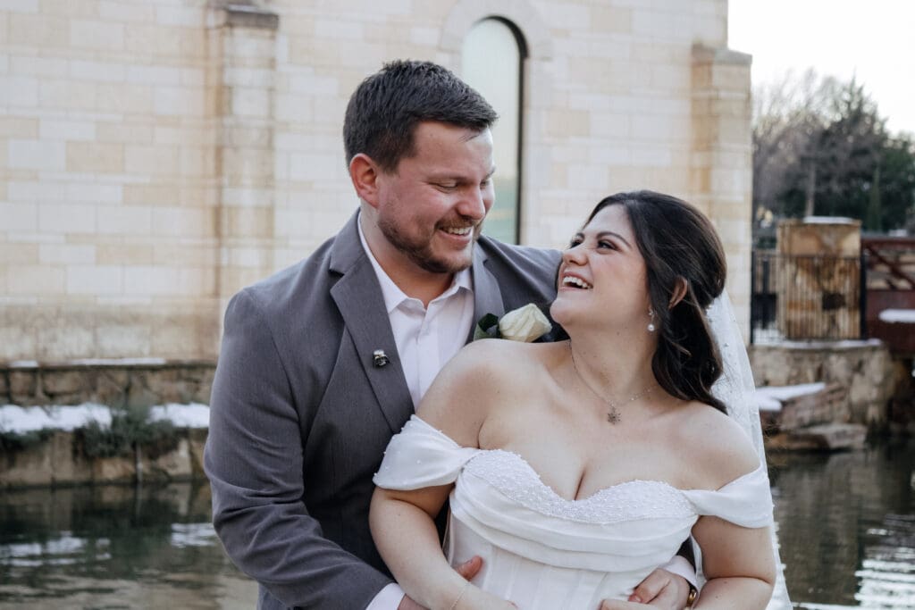 Groom holding bride from behind while they look at each other and laugh